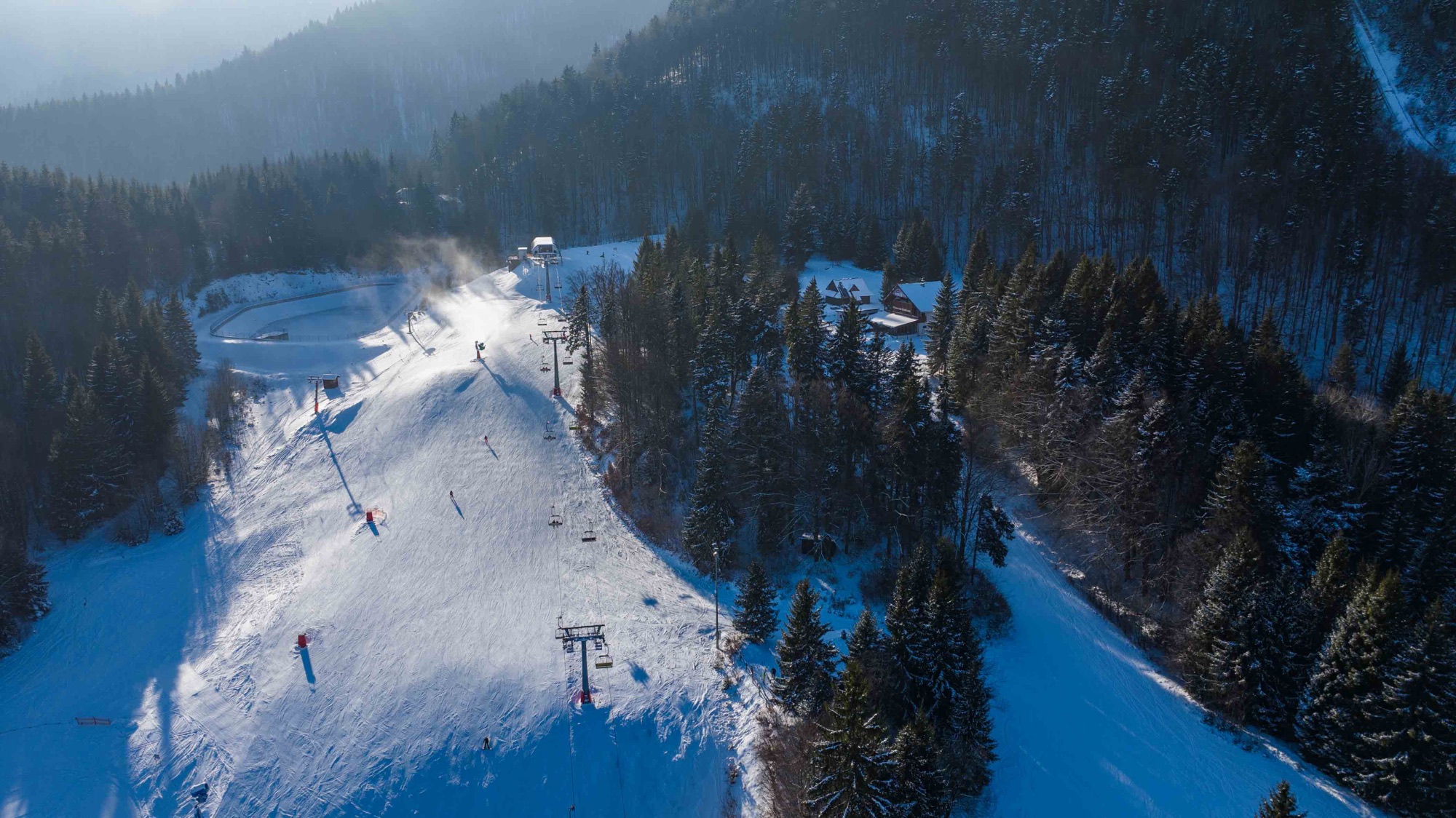 Zasnežená zjazdovka v hmlistom lese z dronu